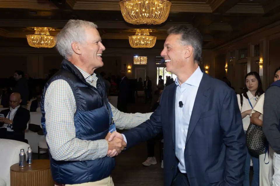 Two guests laughing mid-handshake under the ballroom chandeliers
